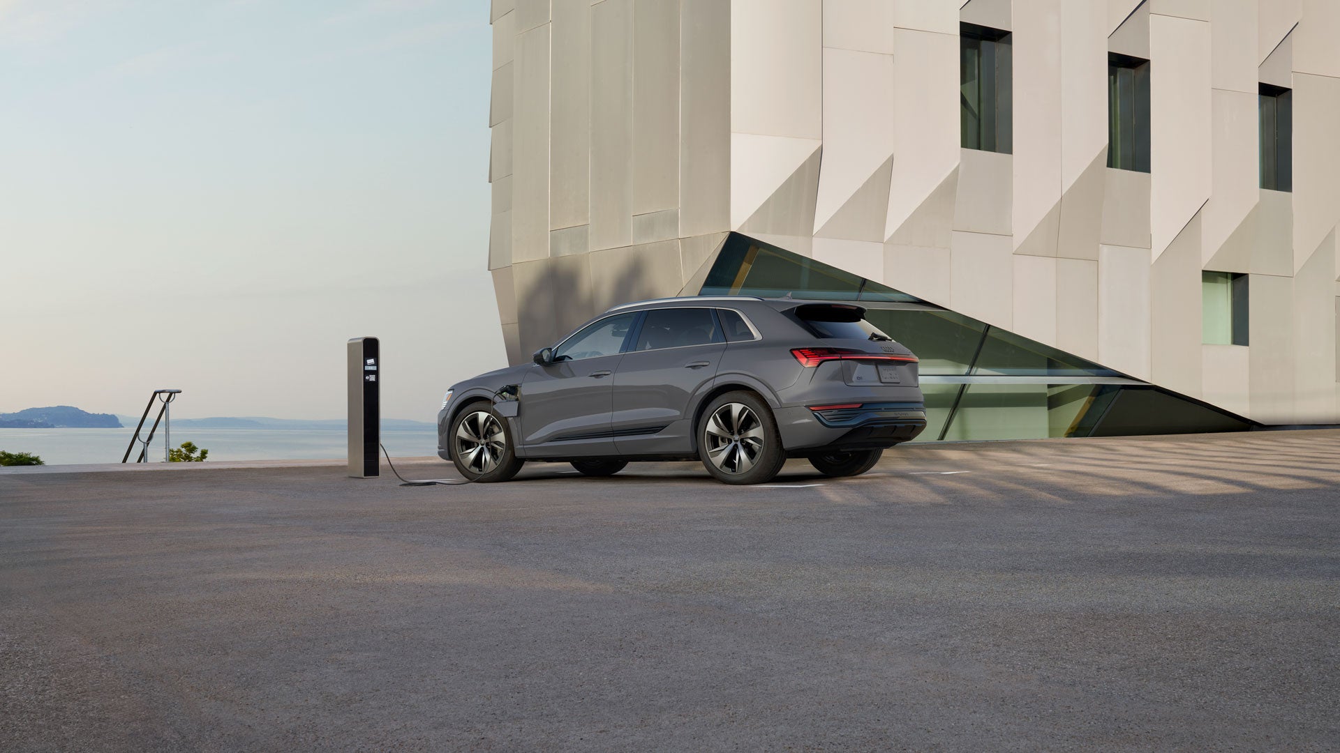 Side view of the 2024 Audi Q8 e-tron charging in front of a building
